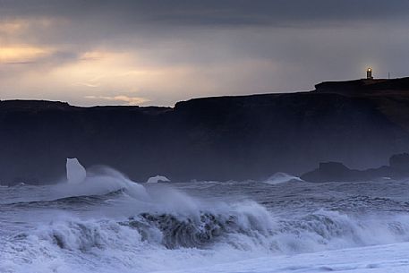 Stormy sea and lighting lighthouse at the Cape Dyrhlaey, Myrdalur, Iceland, Europe